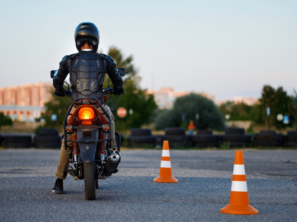 A motorcycle rider at dusk in a parking lot with orange cones.