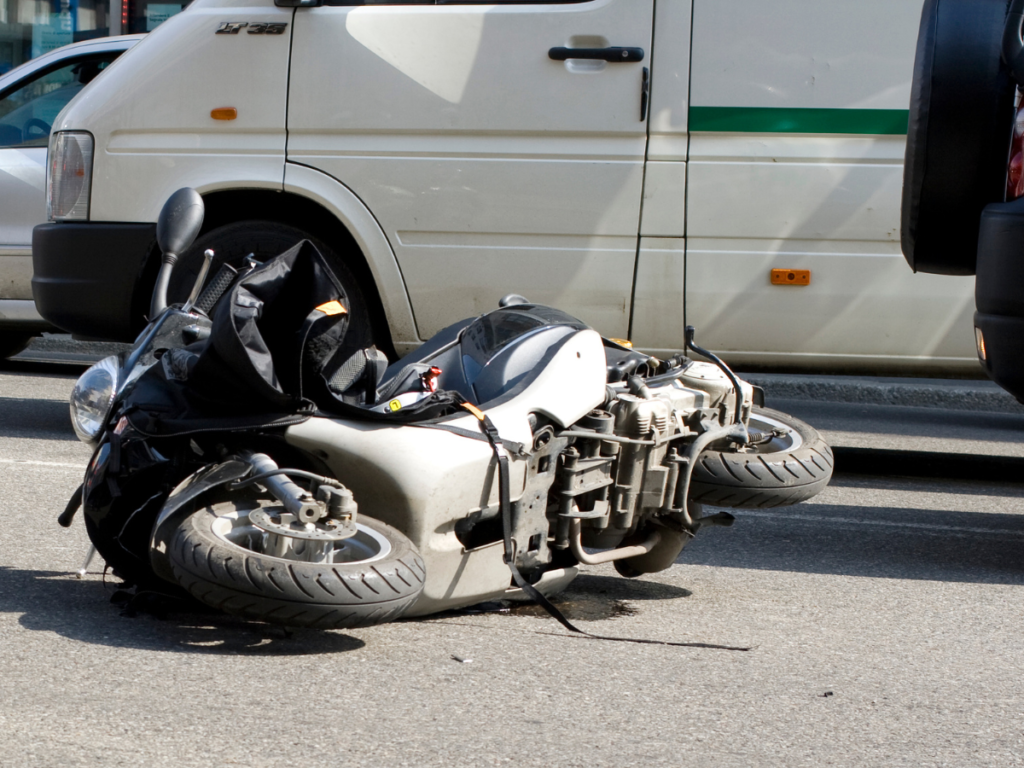 Motorcycle on its side in the middle of the road by a car.