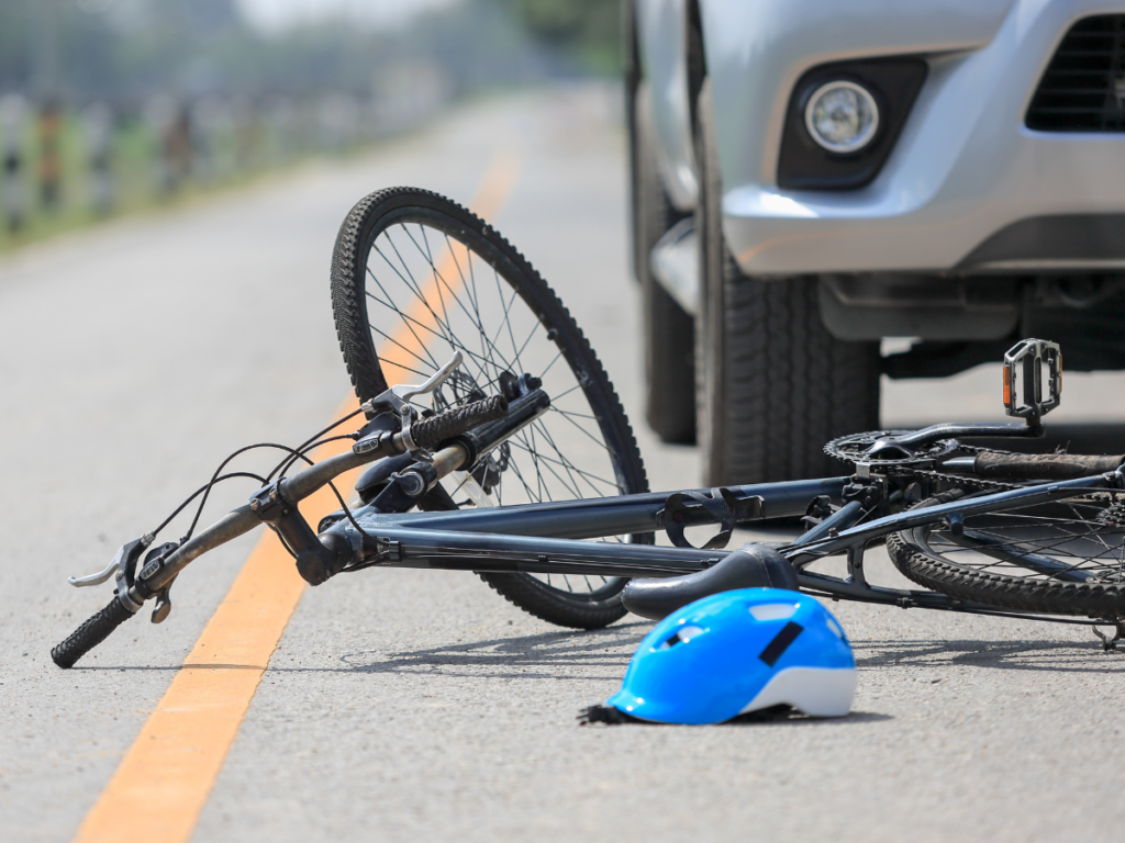 A bike in the middle of the road with a helmet and a car right behind it.